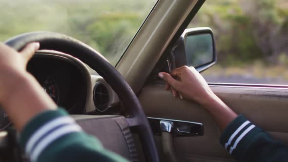 Mid section of woman adjusting side view mirror while driving along country road in convertible car alt