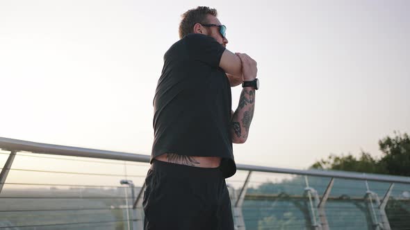 Tattooed Man in Sunglasses Does Exercise on Footbridge alt