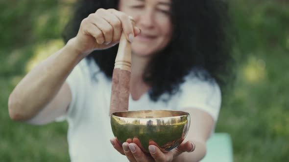 Woman Holding a Bowl and a Wooden Stick Sitting in a Park alt