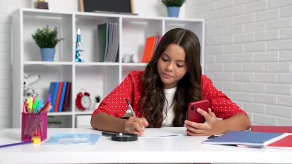 Serious Kid Doing Homework Using Mobile Phone at School Desk Mlearning