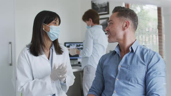 Biracial female dentist with face mask preparing male patient at modern dental clinic alt