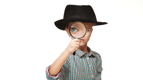 Small Serious Caucasian Kid Girl in Plaid Shirt and Black Hat Looking Through Magnifying Glass on alt