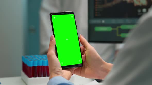 Close Up of Doctor Holding Phone with Green Screen Sitting at Desk alt