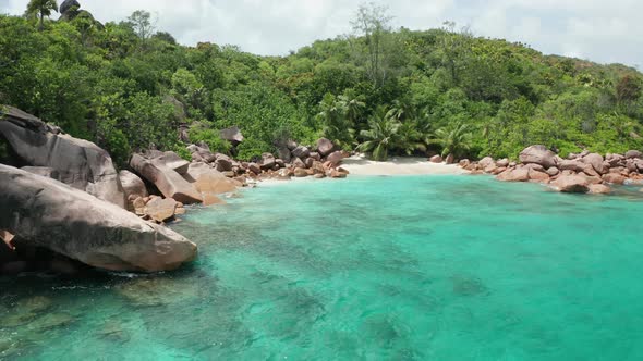 Aerial dolly slowly to small white beach lost between granite boulders