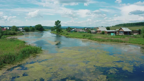 Aerial View. Drone Flies Over River in Village in Sunny Summer Day