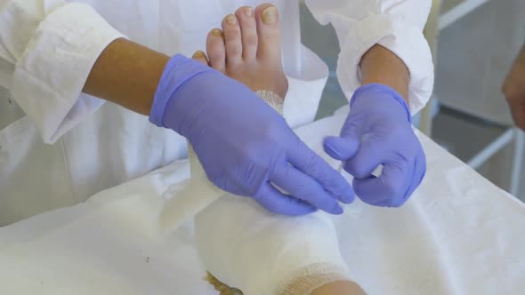 The Doctor's Hands Are Close Up Which Makes a Bandage on the Foot of a Sick Woman alt