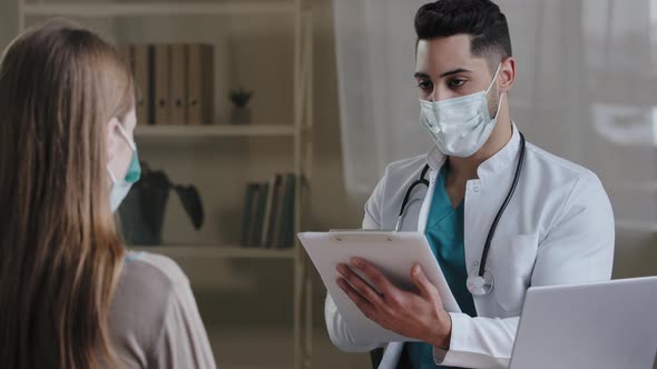 Arabian Male Doctor Physician in Medical Face Mask Making Notes on Clipboard Consulting Female alt