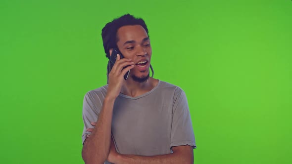 Portrait of Young Male with Long Dreadlocks Talking on Smartphone on Green Screen alt