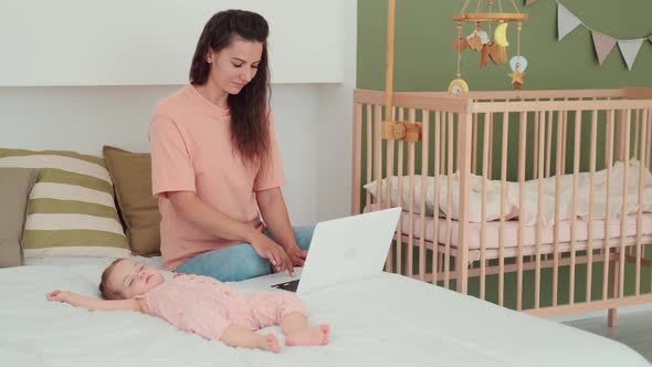 Busy Mom Works Using Laptop While Baby Sleeps Next to Her alt