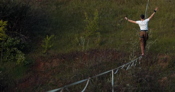 A Man in White Shirt Is Balancing on the Slackline Over the Quarry Extreme alt