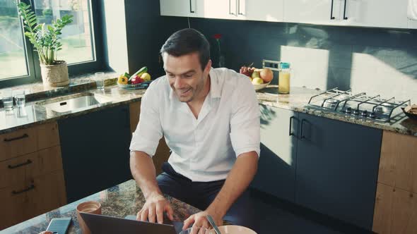 Smiling Man Watching Video on Computer in House. Business Man Getting Good News alt