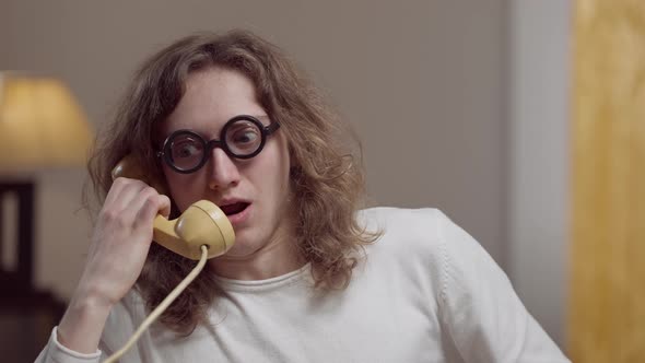 Portrait of Genius Nerd Young Man in Retro Eyeglasses Talking on Vintage Phone Indoors alt