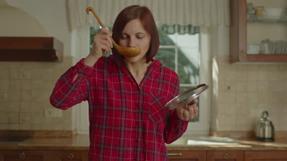 Pretty Woman in Red Shirt Holding Scoop and Pan Lid and Tasting Meal Looking at Camera alt