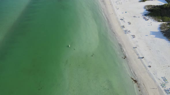 Aerial view moving down the beach showing several beach chairs setup along the water line. The Flori alt