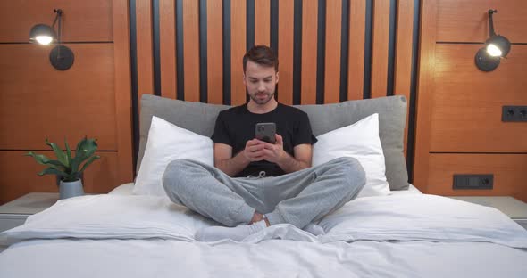 Young Man Sits on the Bed and Playing Game on a Smartphone Man Wins the Game Emotions of Victory alt