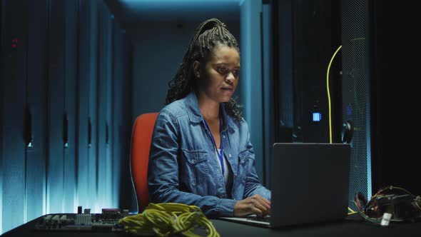 African american female computer technician using laptop working in business server room alt