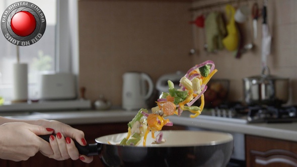 Woman Tossing Vegetables On A Frying Pan In The Kitchen In Slow Motion Shot On Red Camera alt