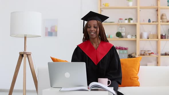 Black Woman in Cap and Gown Waving Greeting Person in Video Call Spbi alt