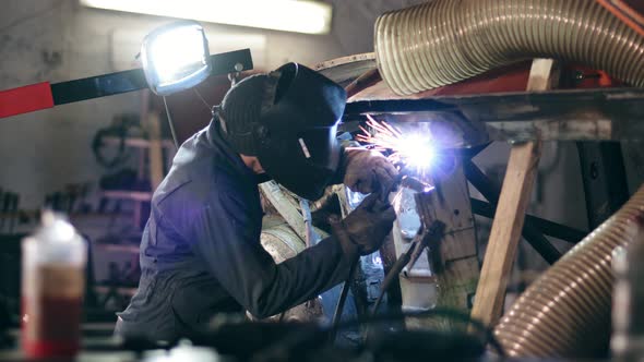 Male Worker at a Welding Factory in a Welding Mask is Working with Metal Construction alt