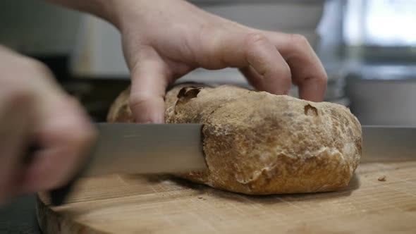 Mens Hands Slice Fresh Crispy Bread on a Wooden Cutting Board