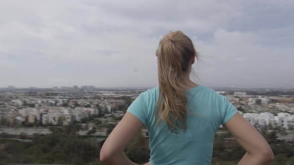 A young woman runner standing at the top of trail overlooking neighborhood. alt