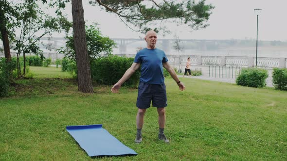 Strong and Healthy Pensioner Performs Gymnastic Exercise in Park Outside alt