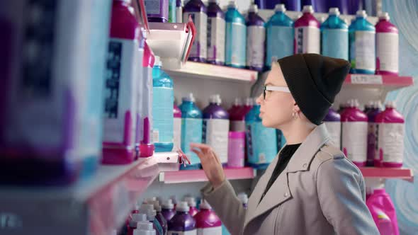 Nice Blonde Girl with Short Haircut in Black Hat and Beige Leather Jacket Chooses Washing Powder alt