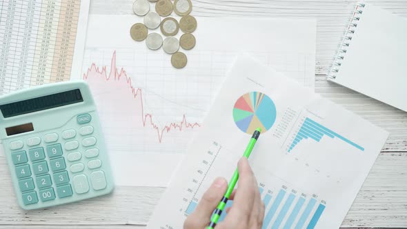 A Businessman is Analyzing Investment Charts with Calculator on the Office Desk Table alt