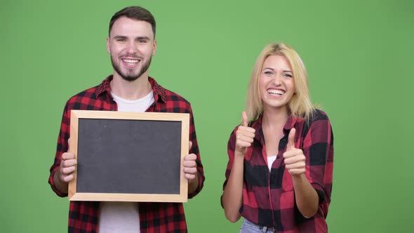 Young Couple Holding Blackboard and Giving Thumbs Up Together