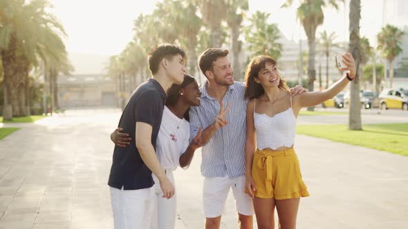Positive Young Multiethnic Friends Making Selfie on Smartphone While Standing on Sunny Embankment alt