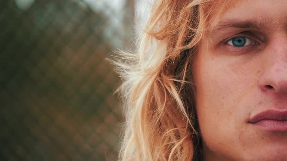 Close up of the attractive male hipster, half face of blue-eyed guy with blond long curly hair