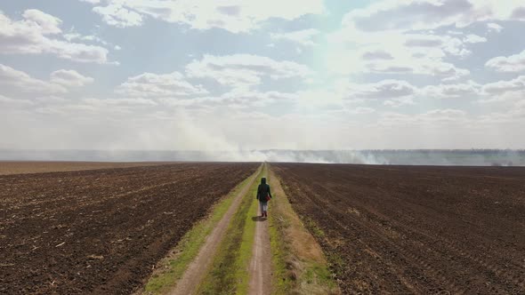 A Girl Walks Along the Road in the Field to the Place Where There is a Fire