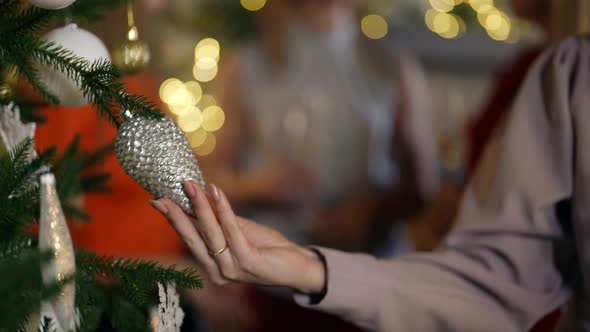 Closeup of a Woman's Hand and a Silver Cone Hanging on a Christmas Tree alt