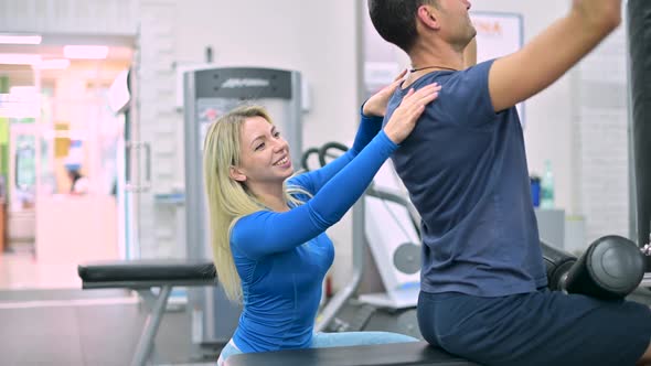 Young woman trainer monitors the correctness of the exercise by the man alt