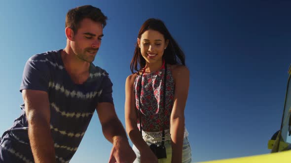 Caucasian couple standing near beach buggy by the sea reading a map alt