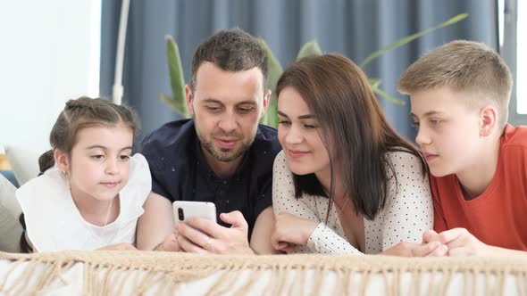 Happy American Family Relaxing on Sofa at Home They Use Smartphone and Have Fun Laughing alt