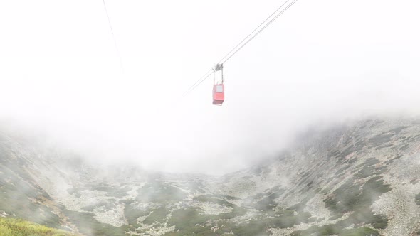 Red mountain cableway car in clouds and fog alt