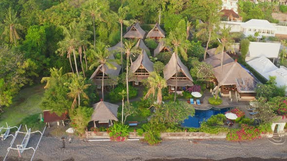 Top View of Tropical Bungalows with Palm Trees and a Blue Oceanfront Pool Next to White Fishing