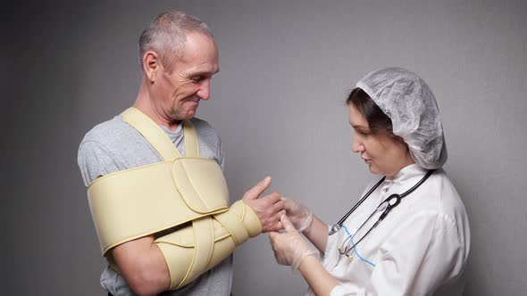 Lady Orthopedist Checks Hand Bones of Old Man with Bandage alt