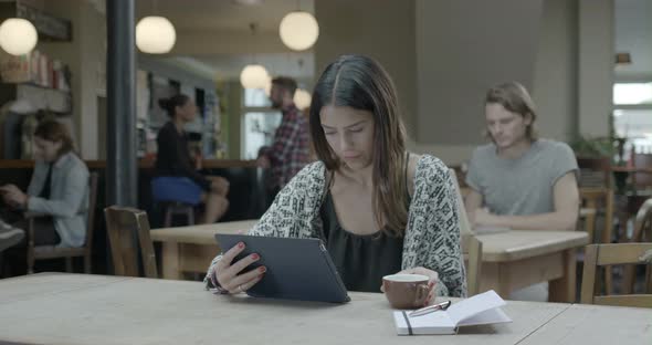 Woman using tablet and drinking coffee in pub