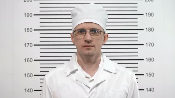 Mugshot of a Doctor in Glasses, in a White Coat, at the Police Station alt