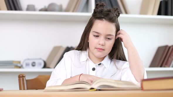 A little girl reads a book in the library alt