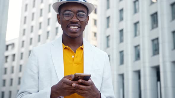 African American man in glasses and suit types on smartphone with cheerful alt
