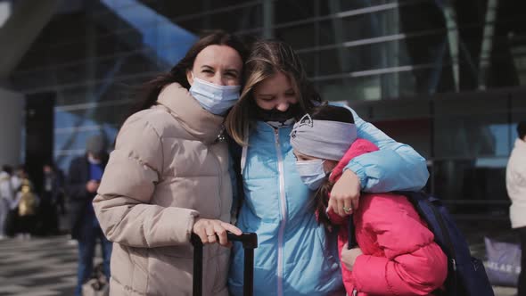A Woman with Two Daughters Outside the Premises in Front of the Airport Terminal with Suitcases and alt