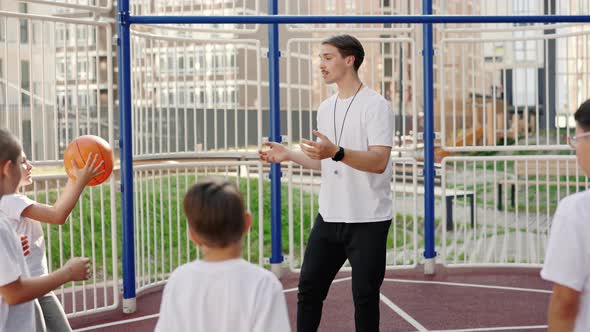 School Coach Mentoring Kids How to Catch and Throw the Ball on Basketball Court Outdoor alt