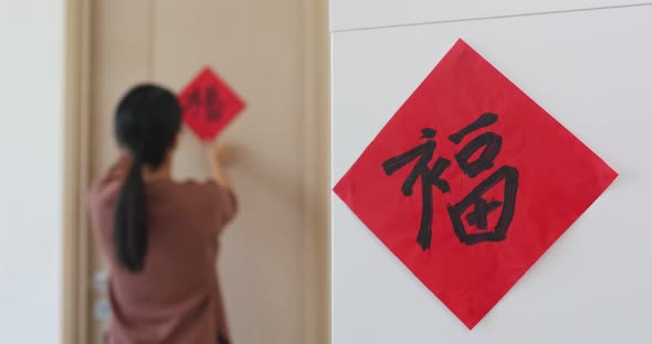 Woman stick chinese red calligraphy on the door for decorating chinese new year, word mean luck alt