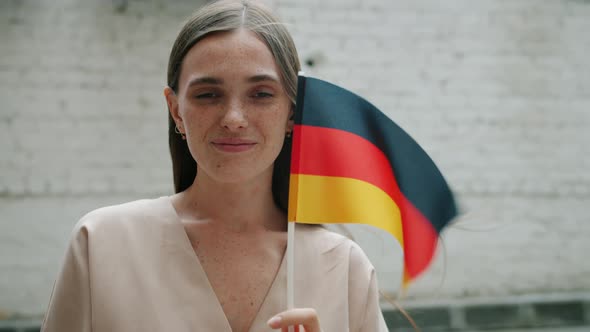 Portrait of Cheerful Woman Holding Official German Flag Looking at Camera Standing Against Brick alt
