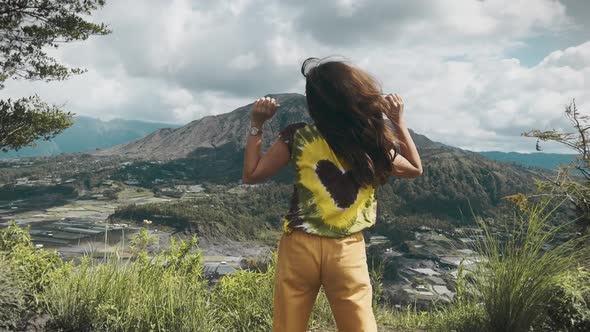 Hippie Girl with Long Dark Hair in Colored Tie Dye Tshirt and Yellow Pants Dances Against alt