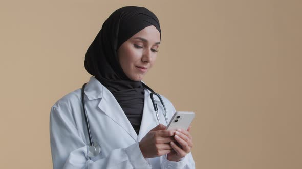 Physician Female Doctor Therapist Woman Wear Hijab White Uniform Standing in Clinic Using Smartphone alt