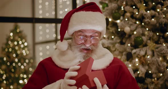 Santa Claus Opens Magic Glowing Gift Box and Looks Inside Bright Light Shines From Box alt
